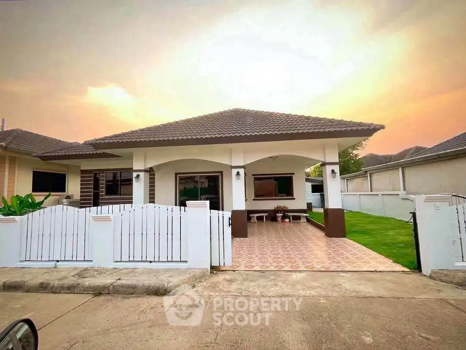 Charming single-story home with tiled patio and lush green lawn at sunset.