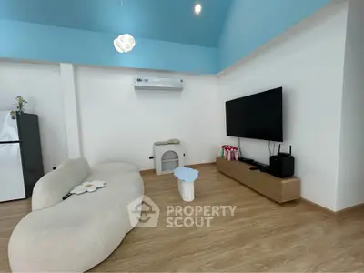 Modern living room with stylish sofa and large TV, featuring a sleek wooden floor and air conditioning.