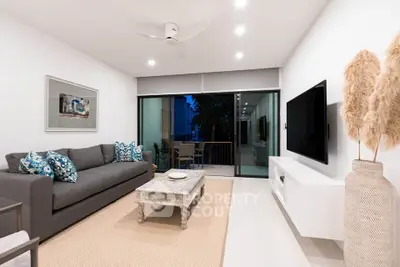 Modern living room with stylish decor and balcony view, featuring a sleek sofa and large TV.