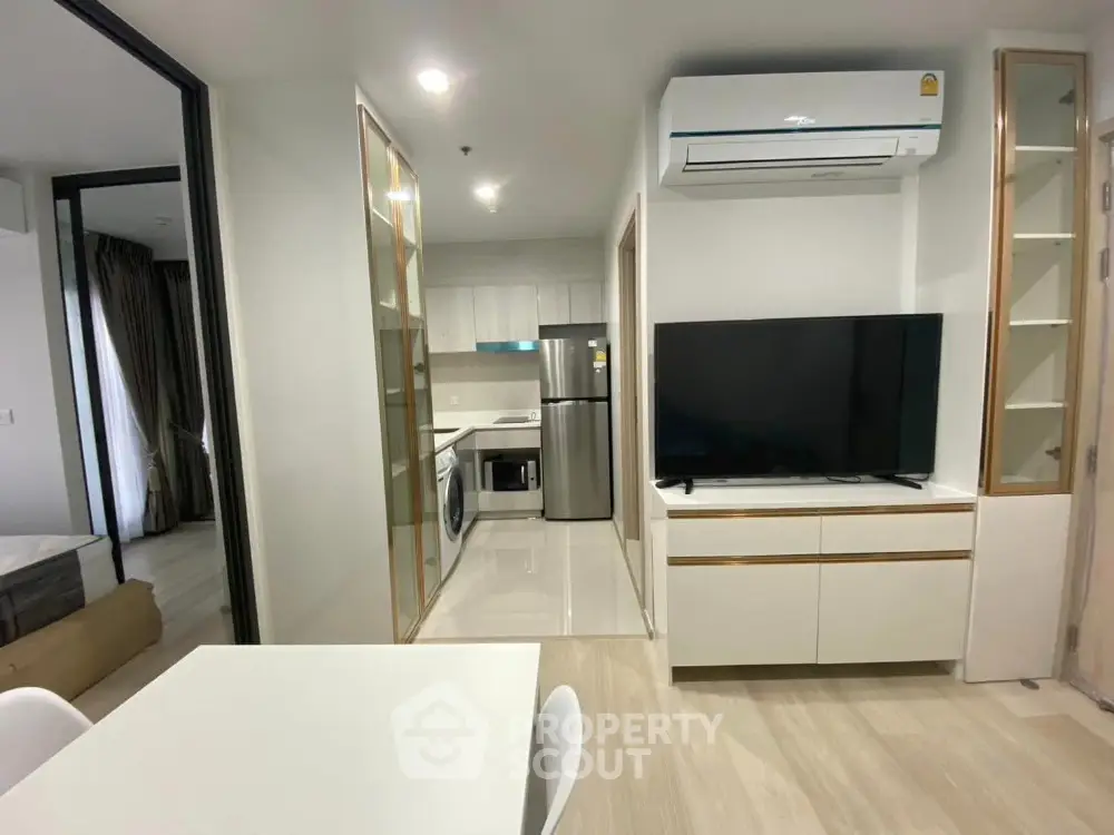 Modern apartment interior with sleek kitchen and spacious living area featuring a large TV and air conditioning.