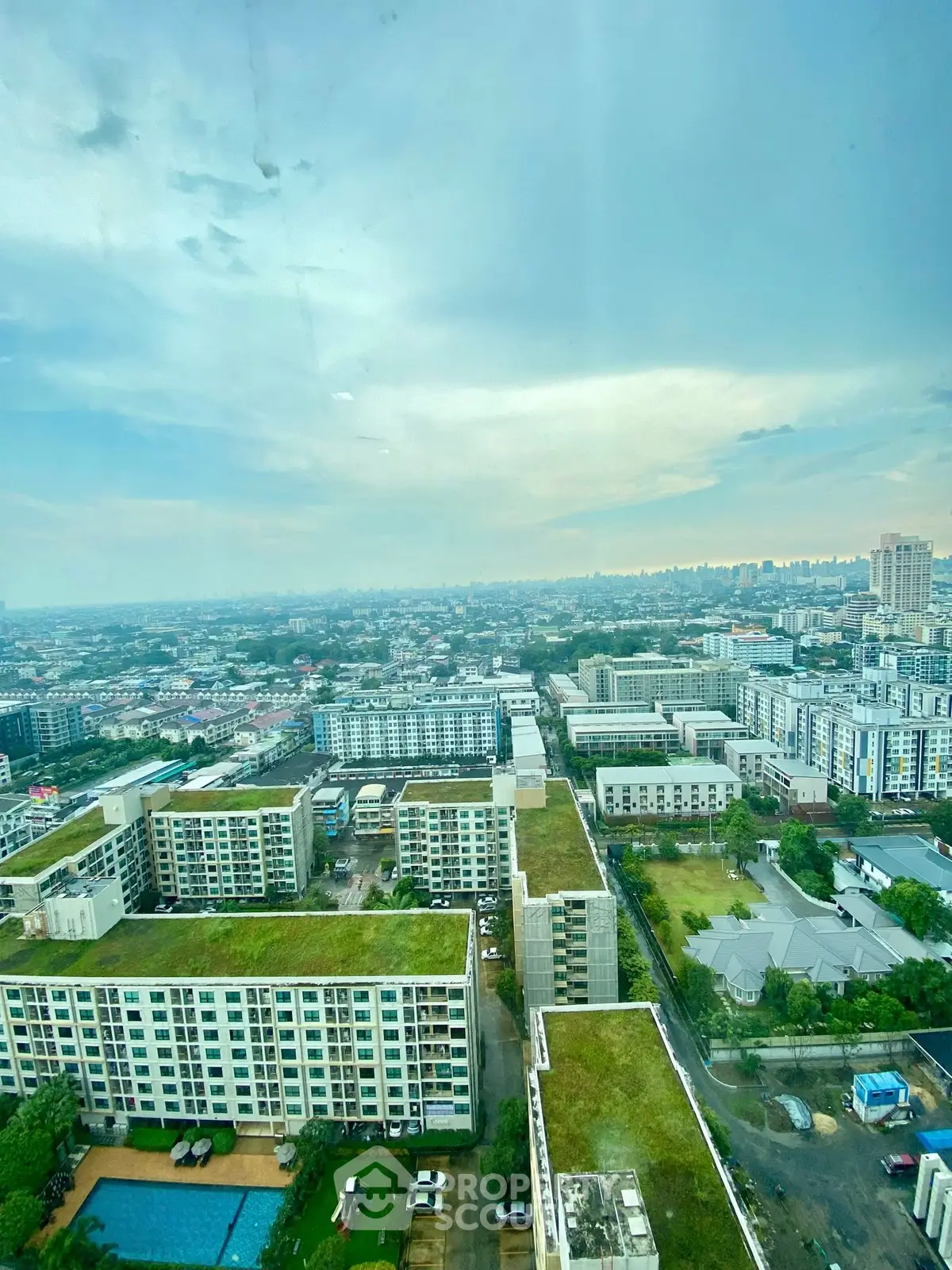 Stunning cityscape view from high-rise building with lush green rooftops and pool area.