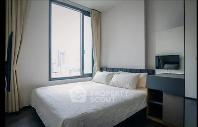 Modern bedroom with large window and city view, featuring a cozy bed and sleek furniture.