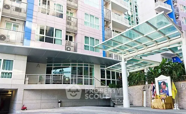 Modern apartment building entrance with glass canopy and landscaped surroundings.