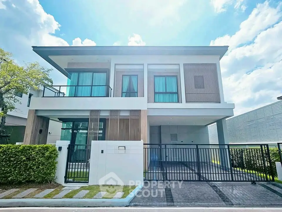 Modern two-story house with large windows and gated driveway under a clear blue sky.