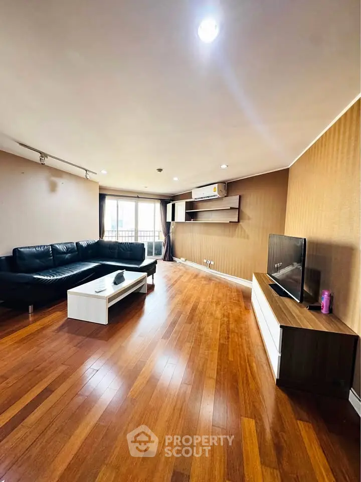 Spacious living room with wooden flooring and modern furnishings in a well-lit apartment.