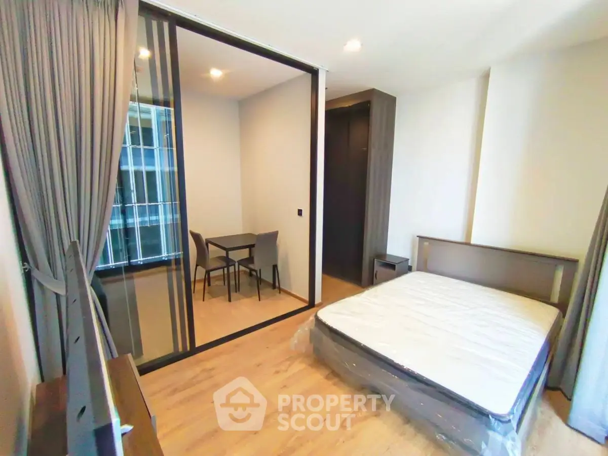 Modern bedroom with glass partition and dining area, featuring sleek design and ample natural light.