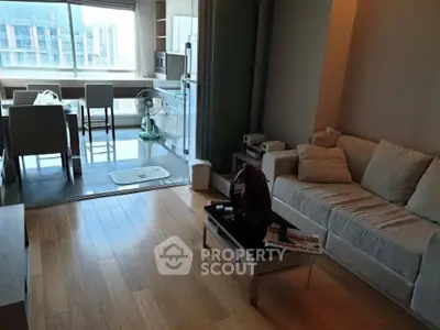 Modern living room with cozy sofa and dining area, featuring large windows and wooden flooring.