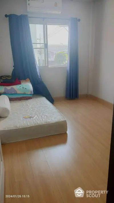 Bright and airy bedroom with gleaming hardwood floors and large window draped with blue curtains, offering a cozy and tranquil living space.