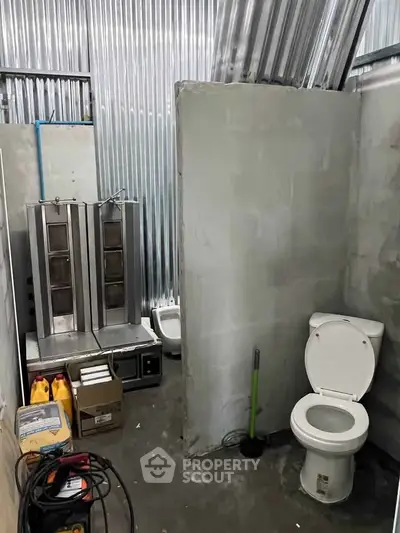 Industrial-style bathroom with corrugated metal walls and basic fixtures.