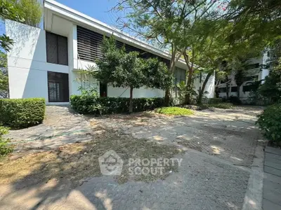 Modern building exterior with lush greenery and paved walkway, showcasing contemporary architecture.