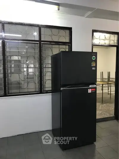 Spacious kitchen area with modern black refrigerator and large windows.