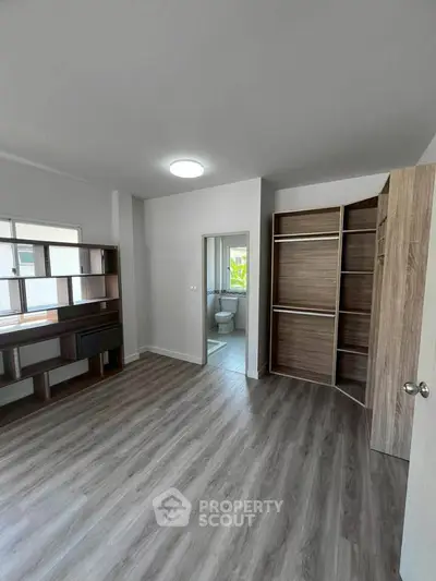 Spacious bedroom with modern closet and en-suite bathroom, featuring sleek wooden flooring.