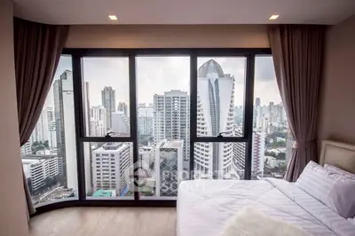 Luxurious bedroom with stunning city view from floor-to-ceiling windows in a high-rise apartment.
