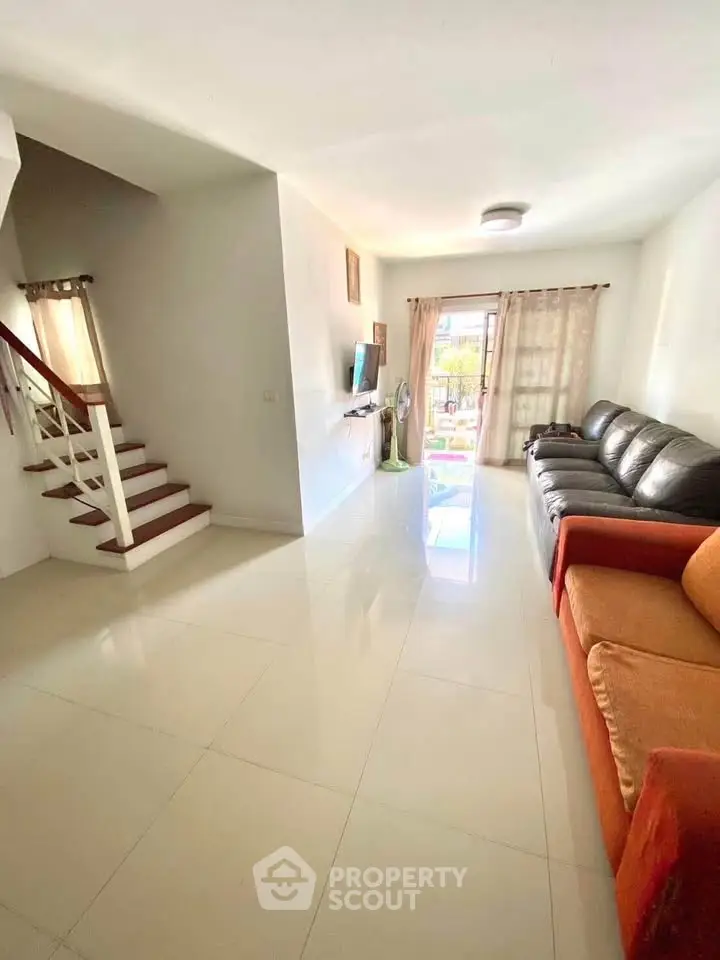 Spacious living room with modern decor and natural light, featuring a cozy seating area and staircase.