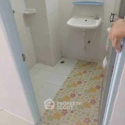 Compact bathroom with floral tile flooring and wall-mounted sink