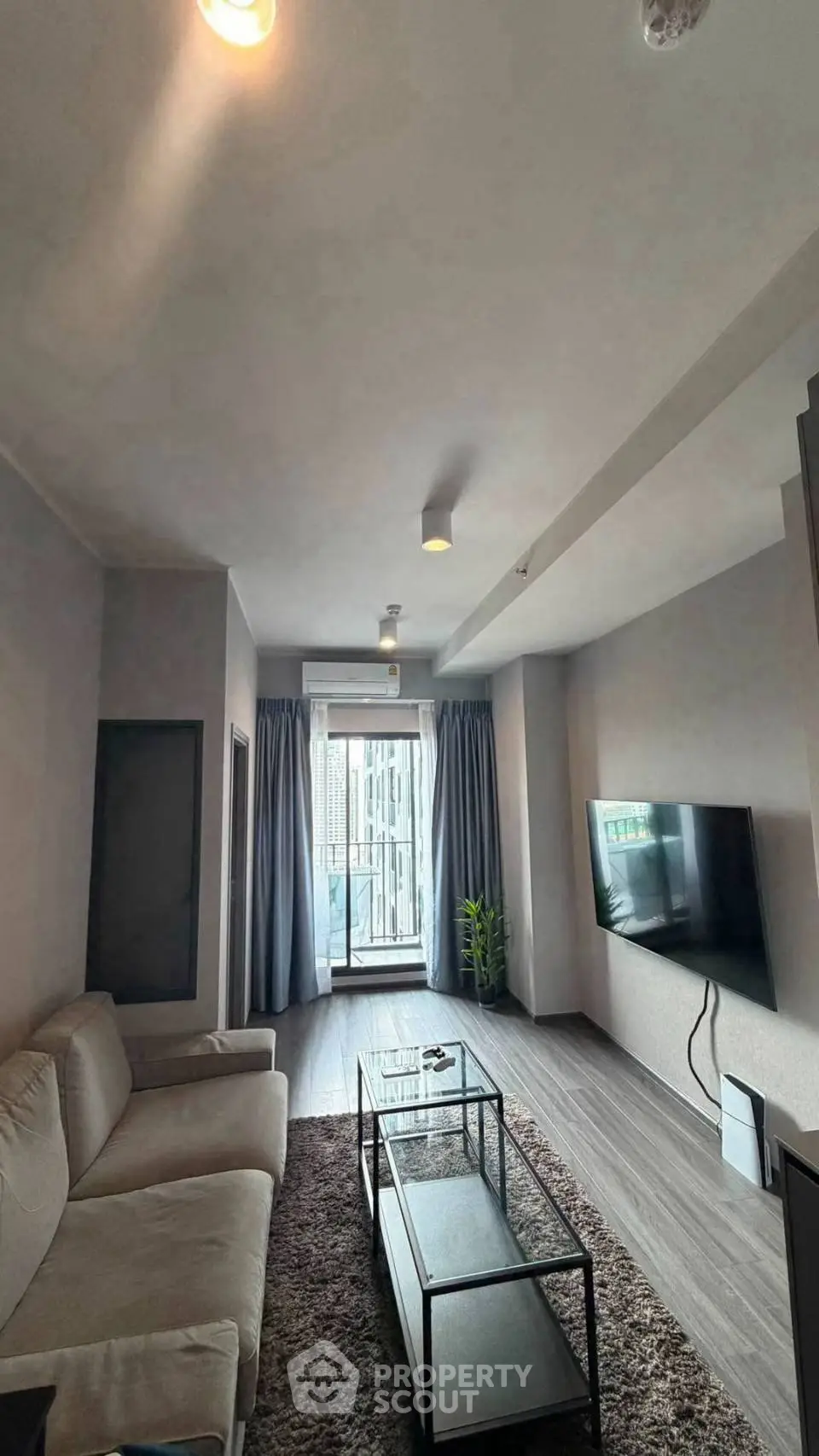 Modern living room with cozy sofa, wall-mounted TV, and balcony view in stylish apartment.