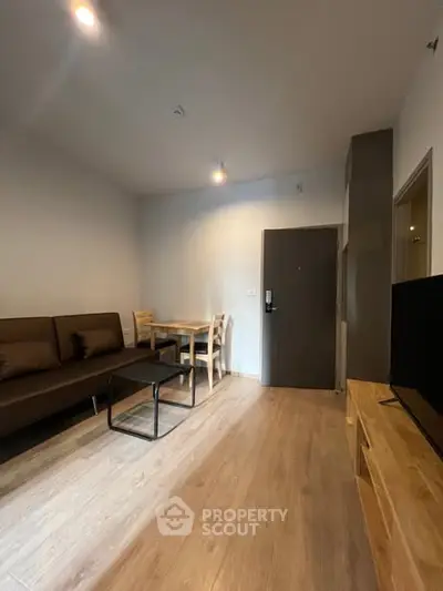 Modern living room with wooden flooring, cozy sofa, dining table, and flat-screen TV.