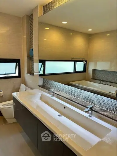 Luxurious modern bathroom with dual sinks and large mirror, featuring elegant tile design and ample natural light.