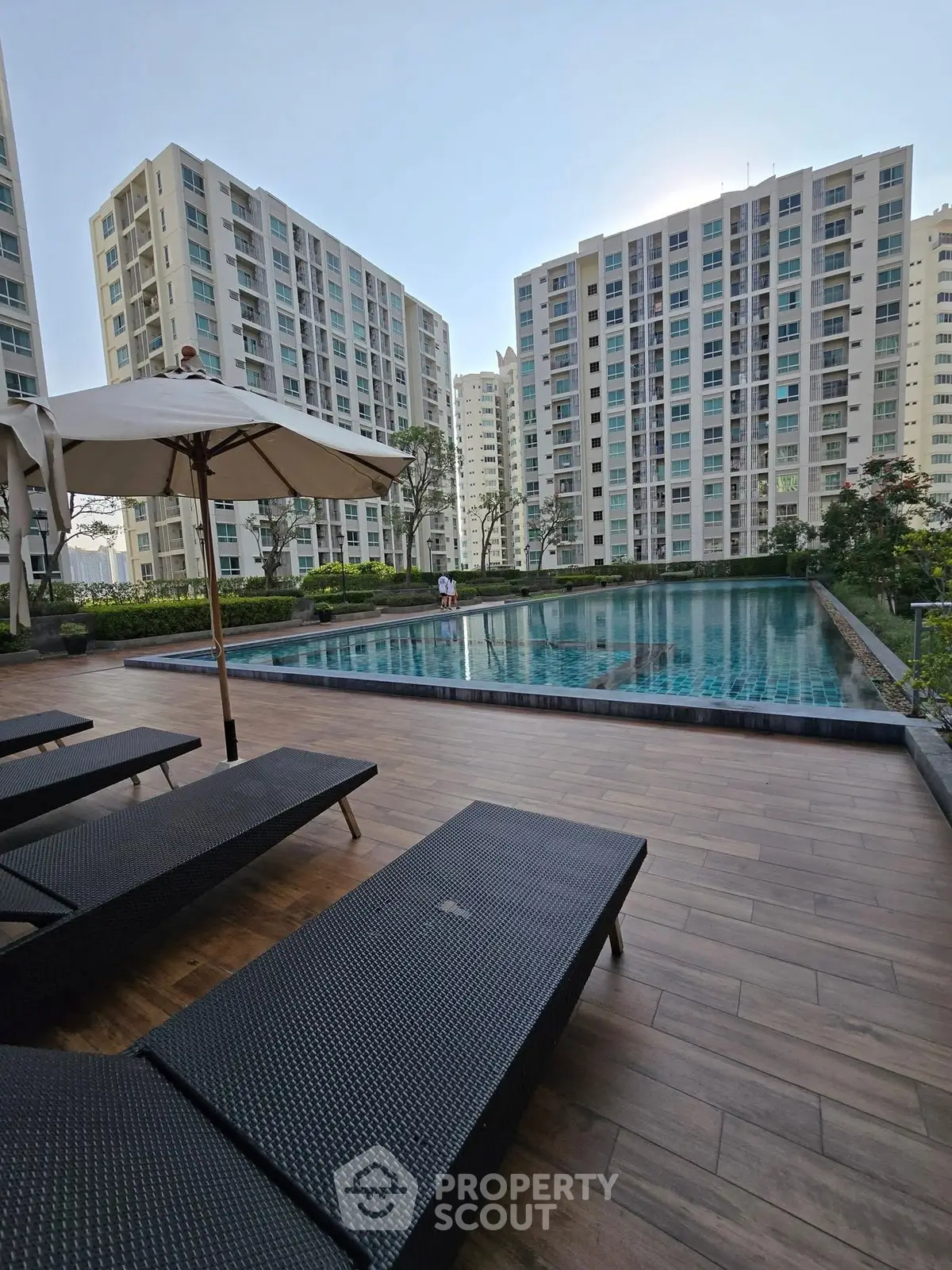 Luxurious apartment complex with poolside relaxation area and modern high-rise buildings.