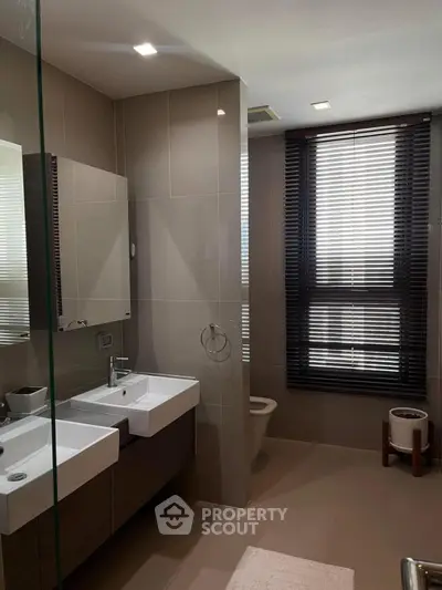 Modern bathroom with dual sinks and large window with blinds, featuring sleek design and ample natural light.