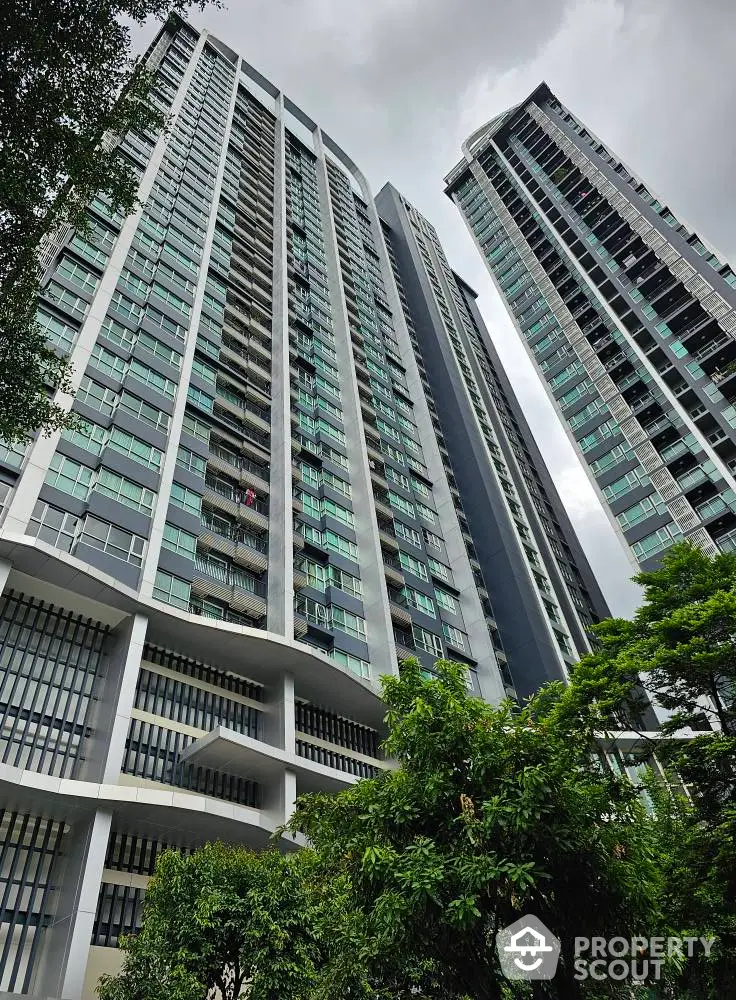 Modern high-rise residential buildings with lush greenery and cloudy sky.