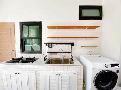 Modern kitchen with gas stove, sink, and washing machine in sleek white design.