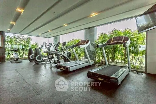 Modern gym with treadmills and exercise bikes in a bright, plant-filled space.