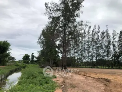Expansive land plot with lush greenery and serene canal view, perfect for development opportunities.