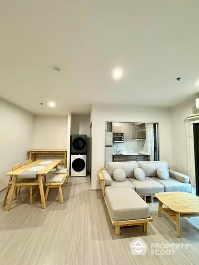 Modern open-plan living room with cozy seating and dining area, featuring a compact kitchen and laundry appliances.