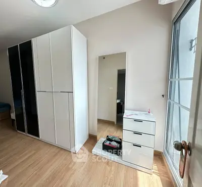 Spacious bedroom with modern white wardrobe and dresser, featuring natural light from large window.