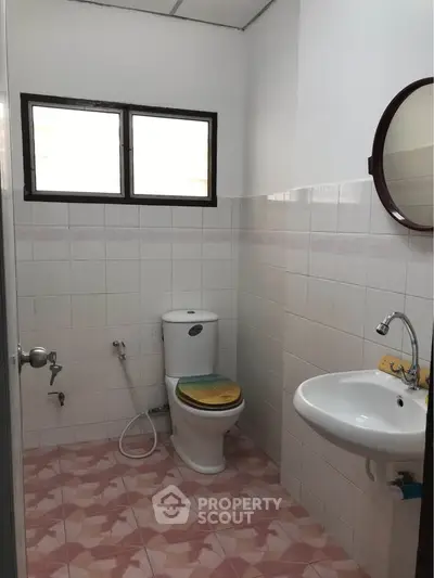 Cozy bathroom with tiled walls and floor, featuring a toilet and sink under natural light.