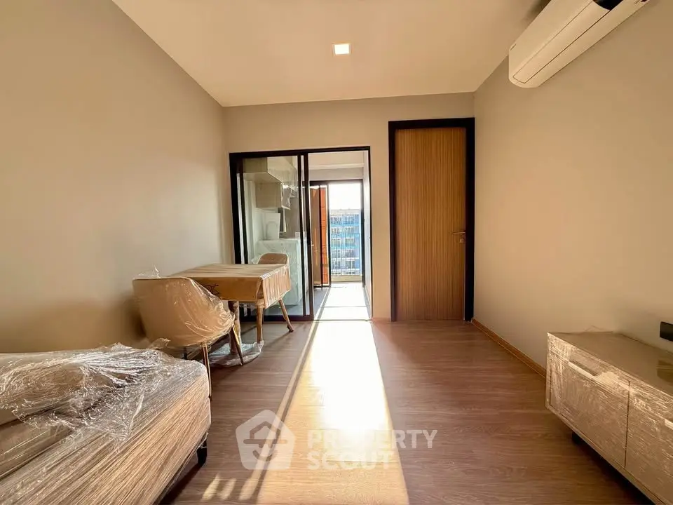 Bright modern living room with wooden flooring and large windows leading to a balcony.