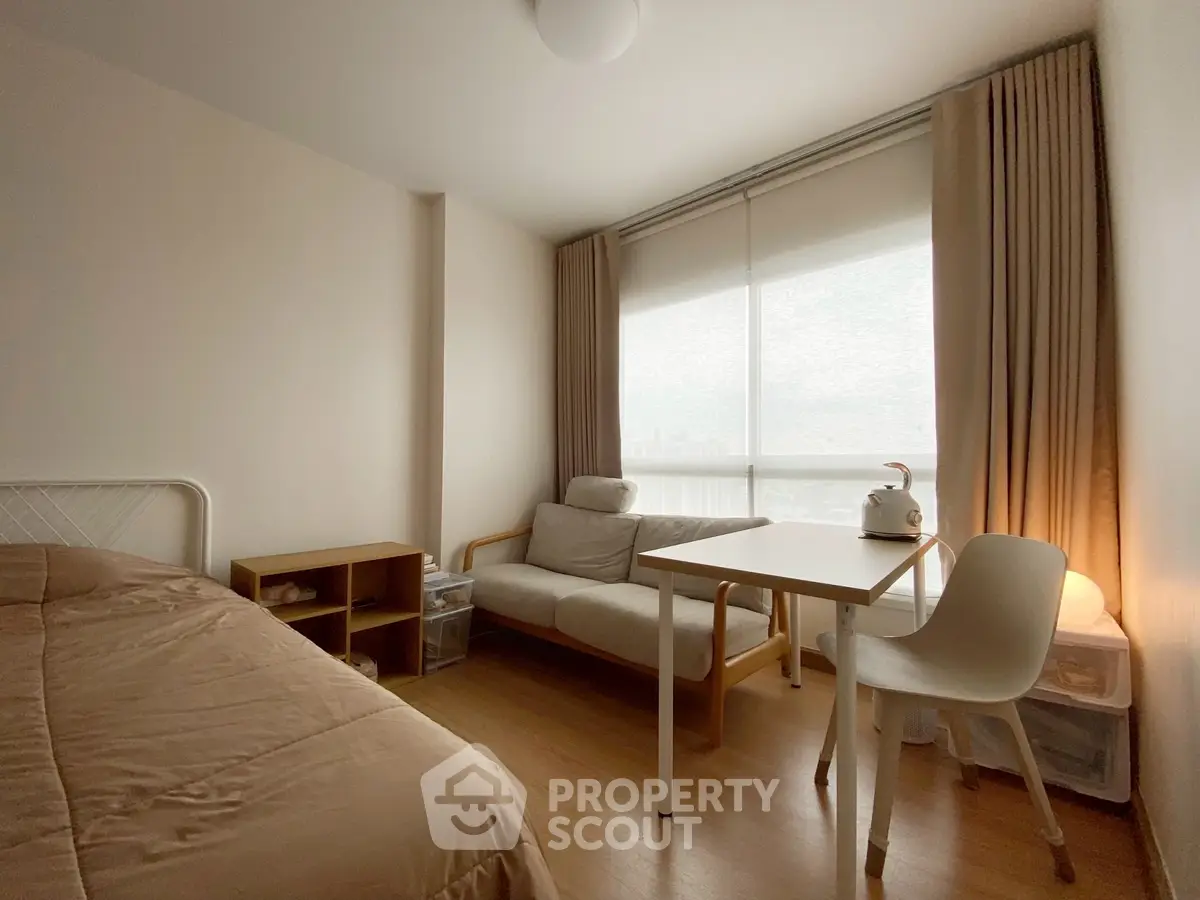Cozy bedroom with natural light, featuring a bed, sofa, and small dining area.