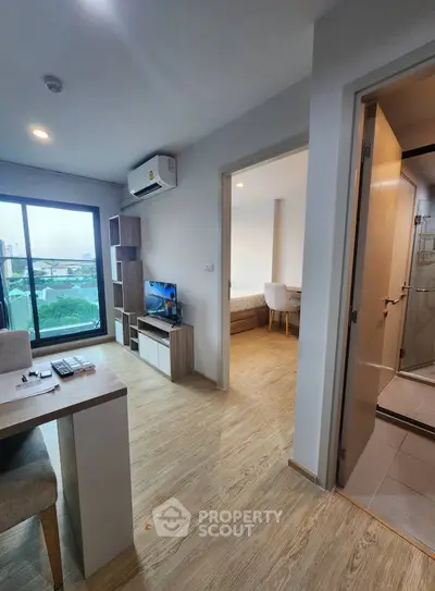 Modern apartment interior with open living area and bedroom, featuring wooden flooring and natural light.
