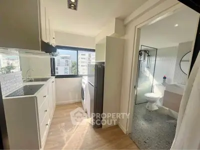 Modern apartment kitchen with open layout and adjacent bathroom, featuring sleek appliances and natural light.
