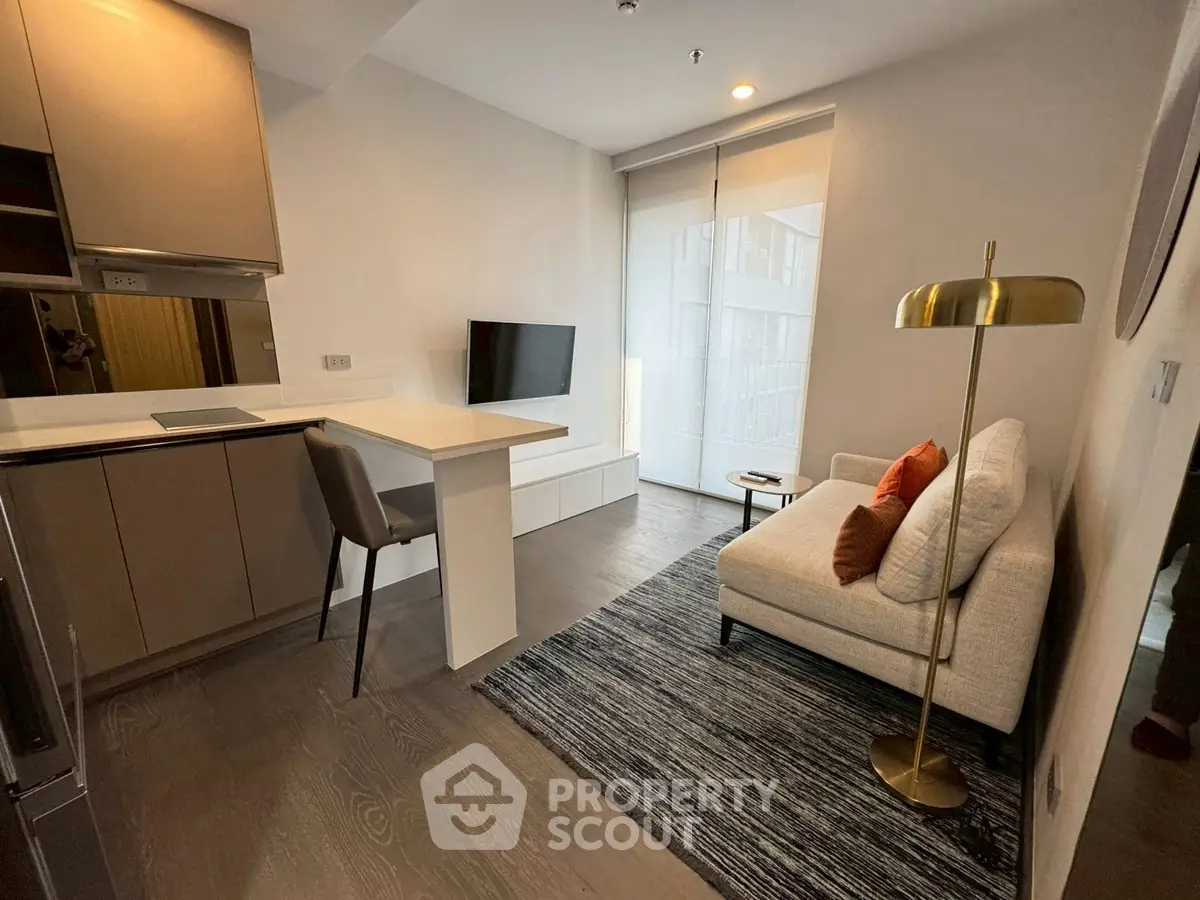 Modern living room with sleek kitchen and cozy seating area, featuring stylish decor and natural light.