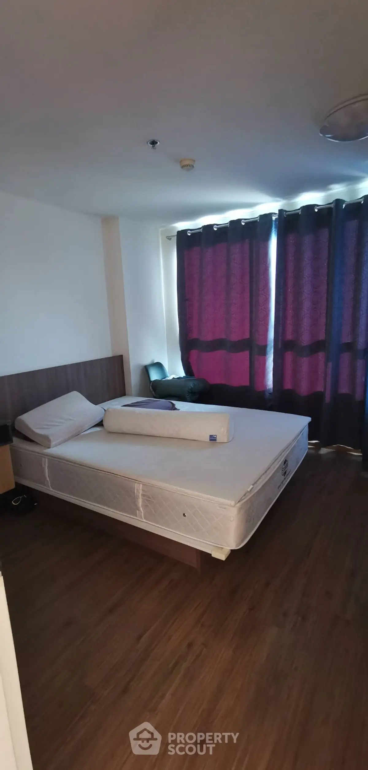 Spacious bedroom with large window and wooden flooring, perfect for cozy living.