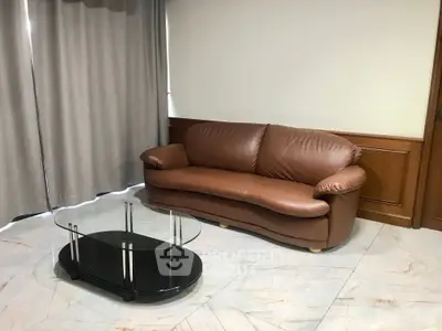 Cozy living room with elegant brown leather sofa and sleek glass coffee table, perfect for relaxation.