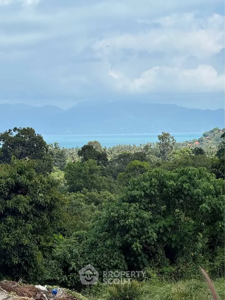 Scenic view of lush greenery and distant mountains with a glimpse of the sea.