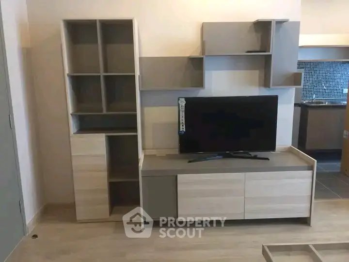 Modern living room with sleek TV stand and shelving, open kitchen in background, stylish and functional design.