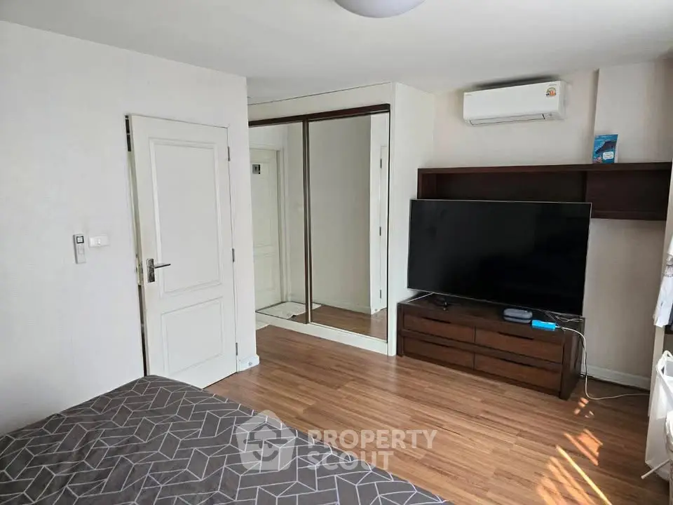 Modern bedroom with wooden flooring, large TV, and mirrored closet doors.