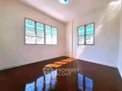 Spacious sunlit room with polished wooden floors and large windows, perfect for a cozy living space.