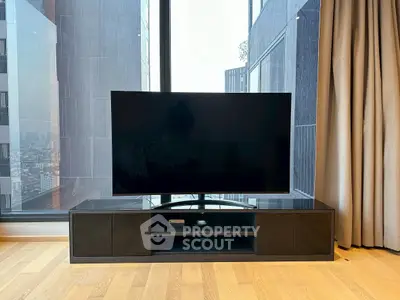 Modern living room with large TV and floor-to-ceiling windows offering city views.