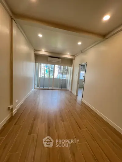 Spacious living room with wooden flooring and large windows offering natural light.