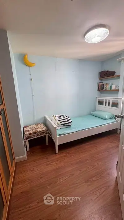Cozy bedroom with wooden flooring and minimalist decor, featuring a single bed and built-in shelves.