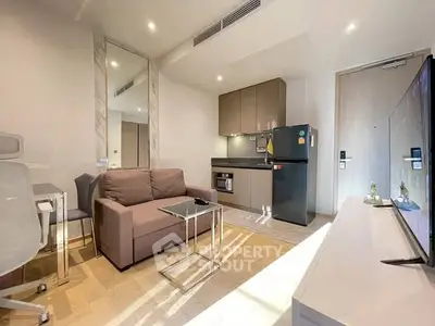 Modern living room with kitchenette, featuring sleek furniture and natural light.