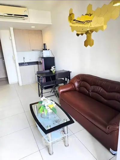 Modern living room with leather sofa, glass coffee table, and compact dining area in a stylish apartment.