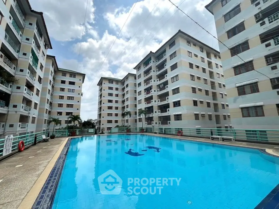 Spacious residential complex with a large swimming pool and modern apartment buildings under a clear sky.