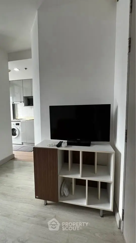 Modern apartment interior with TV stand and kitchen view, featuring sleek appliances and minimalist design.