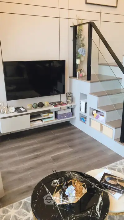 Modern living room with sleek staircase and wall-mounted TV, featuring stylish decor and open shelving.